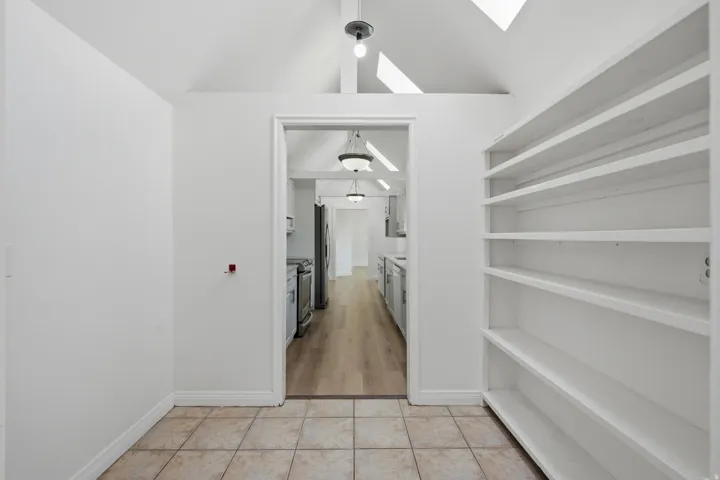 Vaulted ceiling with skylights, built-in shelving, tiled flooring, wood-finish flooring, and recessed lighting