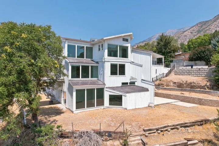 Modern multi-level architecture with extensive window panels, white vertical siding, and a prominent mountain backdrop