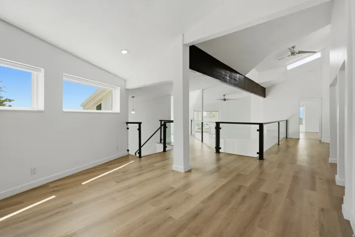 Vaulted ceilings, exposed wood beam, wood-finish flooring, glass panel railing, and modern ceiling fans