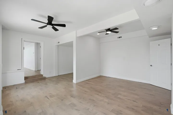 Recessed lighting, wood-finish flooring, two ceiling fans, white paneled doors, and white walls
