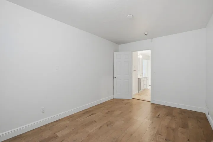 Light wood-finish flooring, white walls, and a white interior door