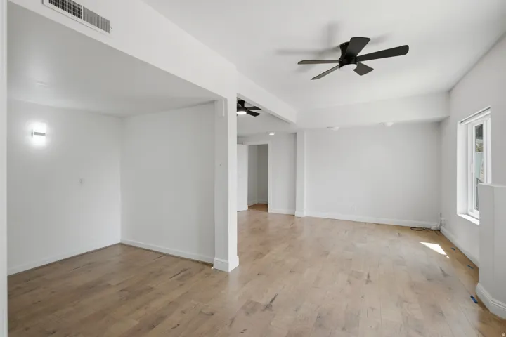Spacious interior with wood-finish flooring, white walls, and a ceiling fan