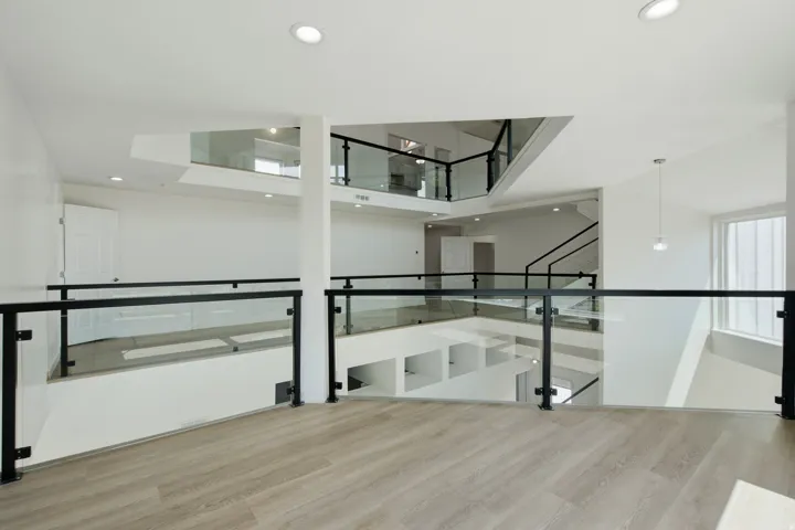 Open-concept interior featuring glass and black metal railings, wood-finish flooring, recessed lighting, and a pendant light fixture