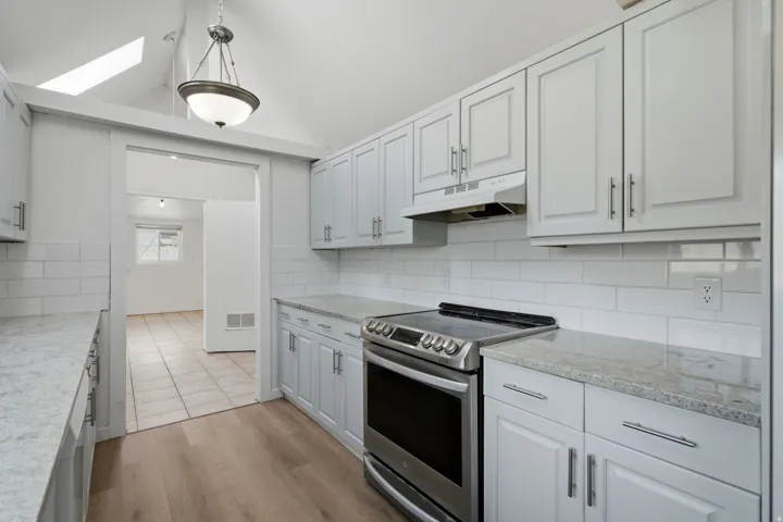 Kitchen featuring wood-finish flooring, white subway tile backsplash, light grey cabinetry, stainless steel range, and granite-style countertops
