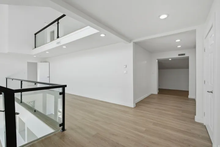 Open-concept living area featuring wood-finish flooring, recessed lighting, and a glass and black metal railing system
