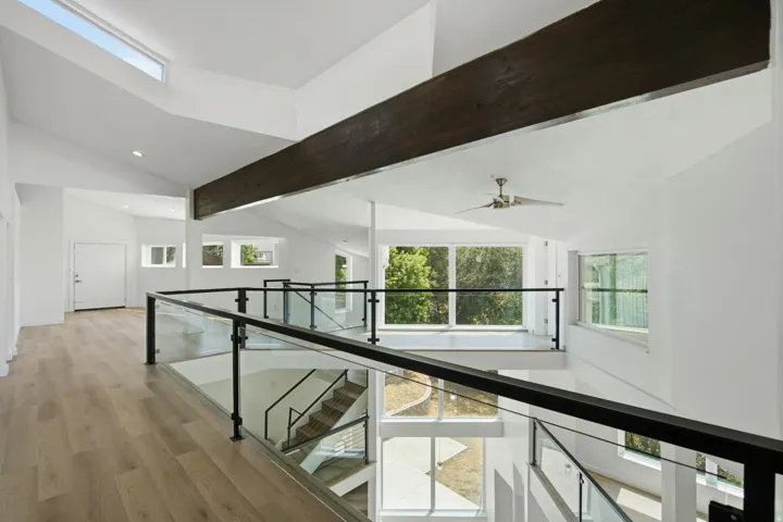 Open-concept interior featuring wood-finish flooring, a prominent exposed beam, a skylight, a glass and metal railing system, and a ceiling fan