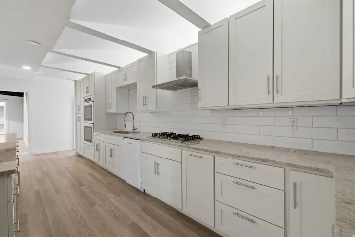 Kitchen featuring wood-finish flooring, white cabinetry, integrated double ovens, a gas cooktop, and light-toned countertops