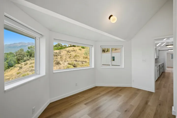 Vaulted ceiling with exposed beam, wood-finish flooring, white walls, and multiple windows