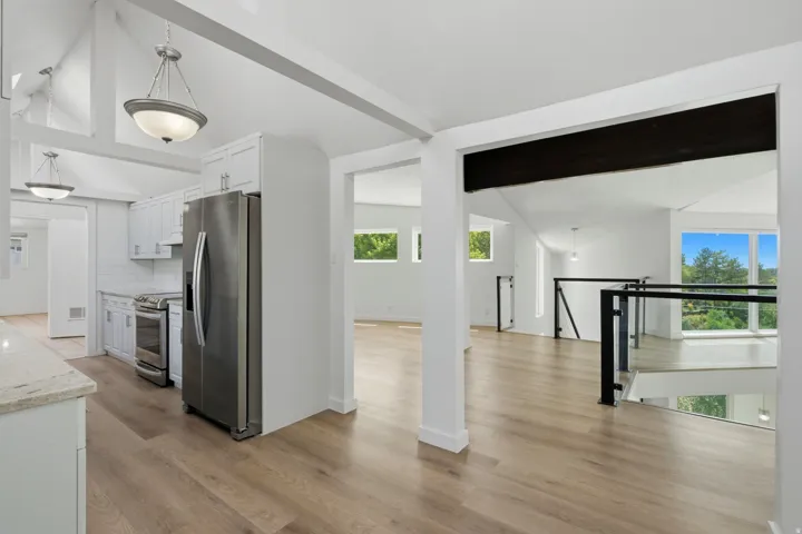 Vaulted ceilings with exposed beams, wood-finish flooring, white cabinetry, stainless steel appliances, and a glass-paneled railing