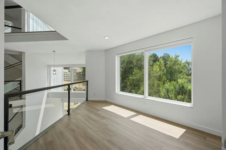 Spacious interior featuring large windows, light wood-finish flooring, recessed lighting, and a glass and metal railing system
