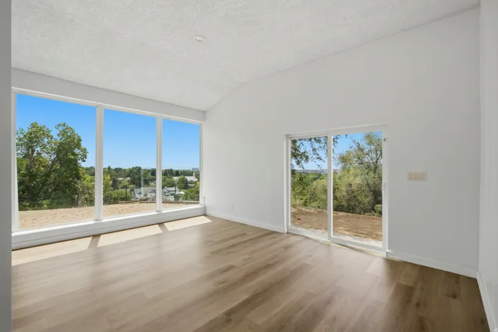 Vaulted ceiling, expansive windows, wood-finish flooring, white walls, sliding glass door