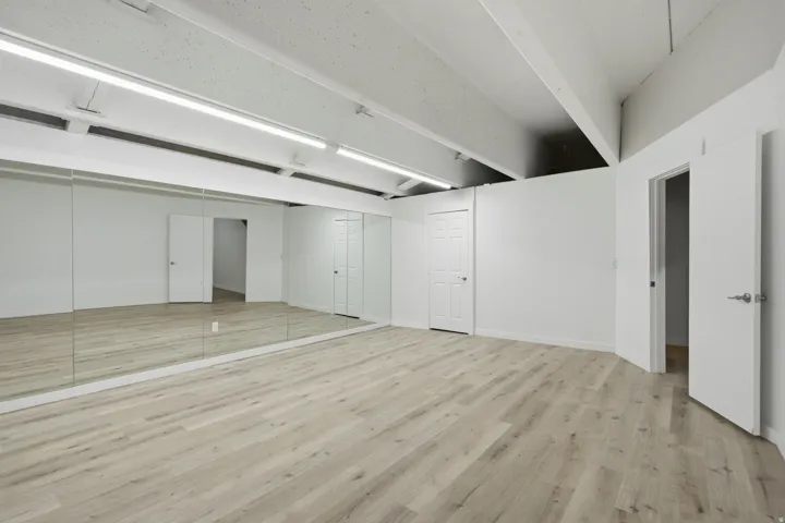 Expansive room featuring wood-finish flooring, full-wall mirrors, exposed ceiling beams, and recessed lighting