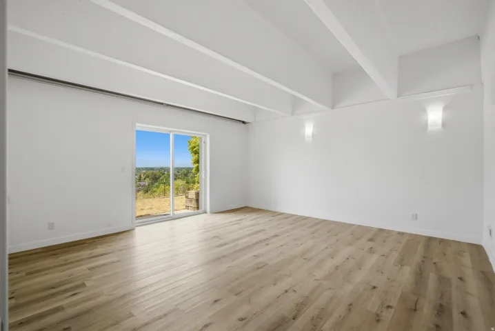 White walls, exposed ceiling beams, wood-finish flooring, sliding glass door, and two wall sconces