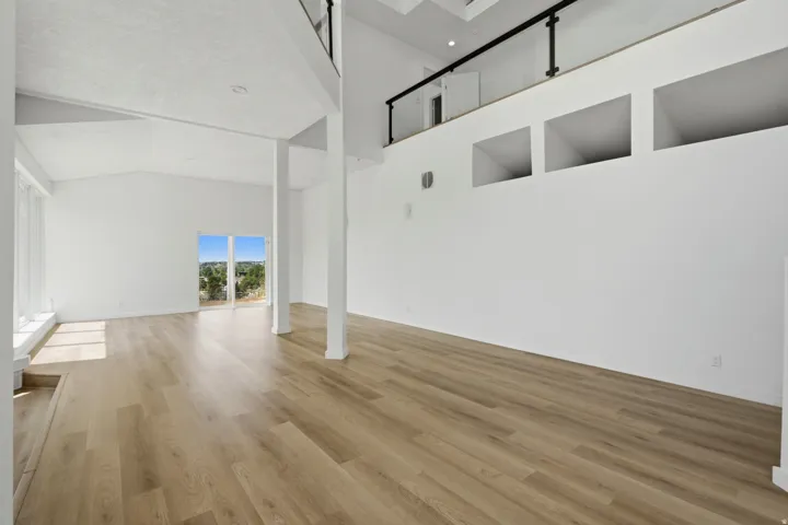 Wood-finish flooring, high vaulted ceilings, expansive windows, multiple recessed wall niches, and a loft with a black metal railing