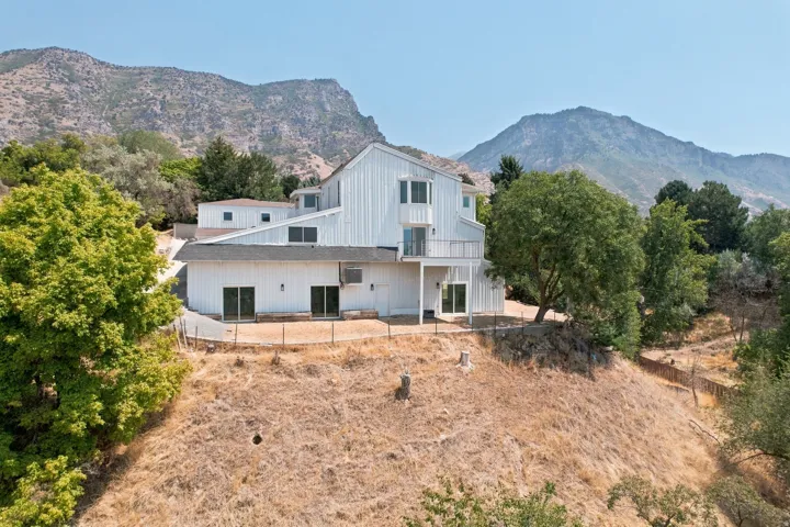 Multi-level residence featuring white vertical siding, multiple sliding glass doors, and an upper-level balcony
