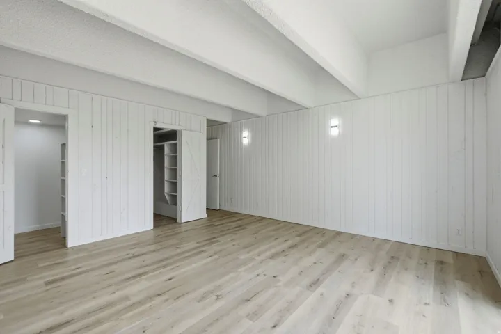 Light wood-finish flooring, white shiplap walls, exposed ceiling beams, built-in shelving, and wall sconces