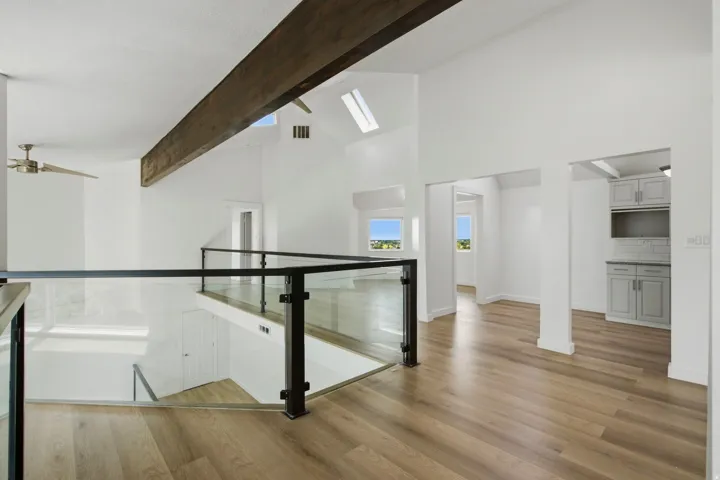 Vaulted ceilings with exposed wood beam, skylights, wood-finish flooring, glass panel railing, and built-in cabinetry