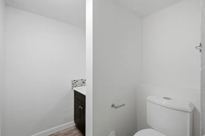 Compact vanity with dark wood-finish cabinetry, mosaic tile backsplash, and wood-look flooring