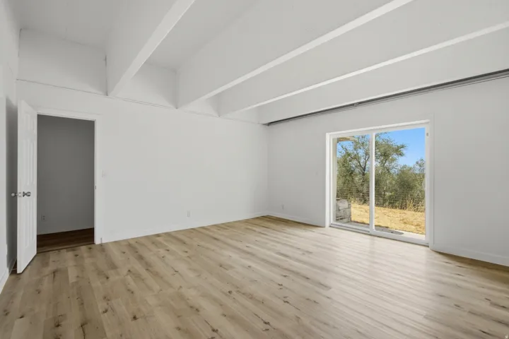 Exposed ceiling beams, wood-finish flooring, white walls, and a sliding glass door