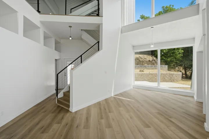 Soaring ceilings with clerestory windows, wood-finish flooring, a modern open-tread staircase with black metal railings, and a two-story window wall