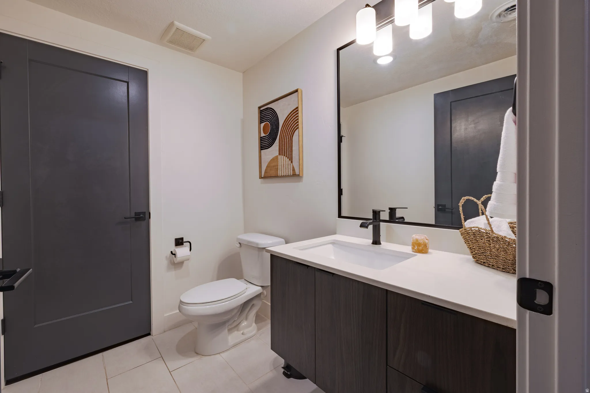Powder Bathroom: Modern vanity with white countertop and integrated sink, matte black faucet, dark wood-finish cabinetry, rectangular framed mirror, and white tile flooring
