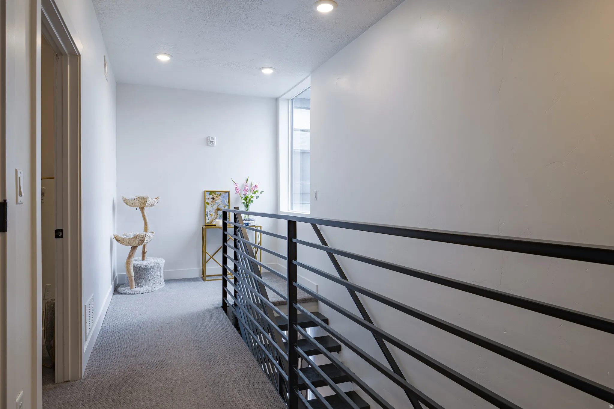 Hallway featuring recessed lighting, light gray carpet, and a modern metal railing