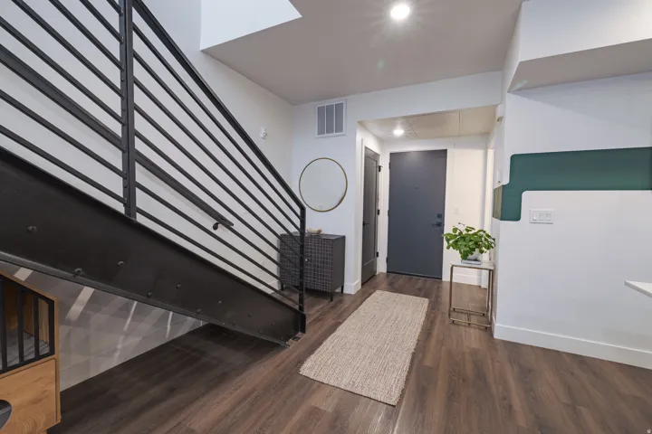 Modern staircase with metal railing, wood-finish flooring, recessed lighting, and a dark-paneled door
