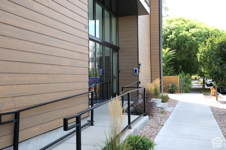 Modern exterior featuring wood-finish siding, full-light entry doors, and a concrete ramp with black metal railings; secure entry requires a digital key.