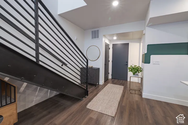 Modern staircase with metal railing, wood-finish flooring, recessed lighting, and a dark-paneled door