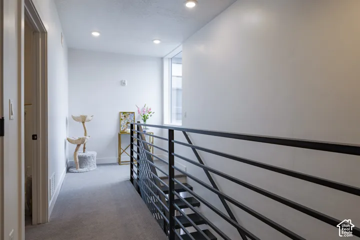 Hallway featuring recessed lighting, light gray carpet, and a modern metal railing