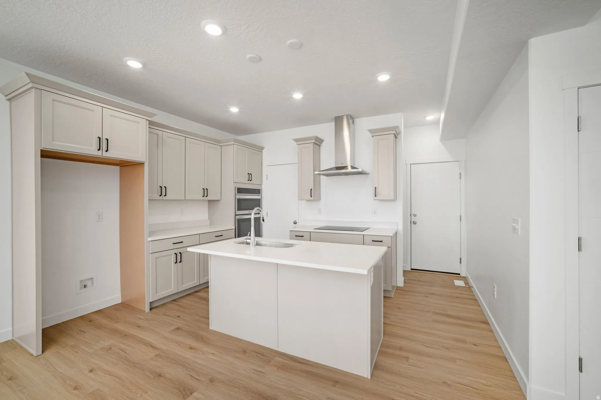 Kitchen featuring light wood-finish flooring, white perimeter cabinetry, a center island with an integrated sink, and stainless steel appliances