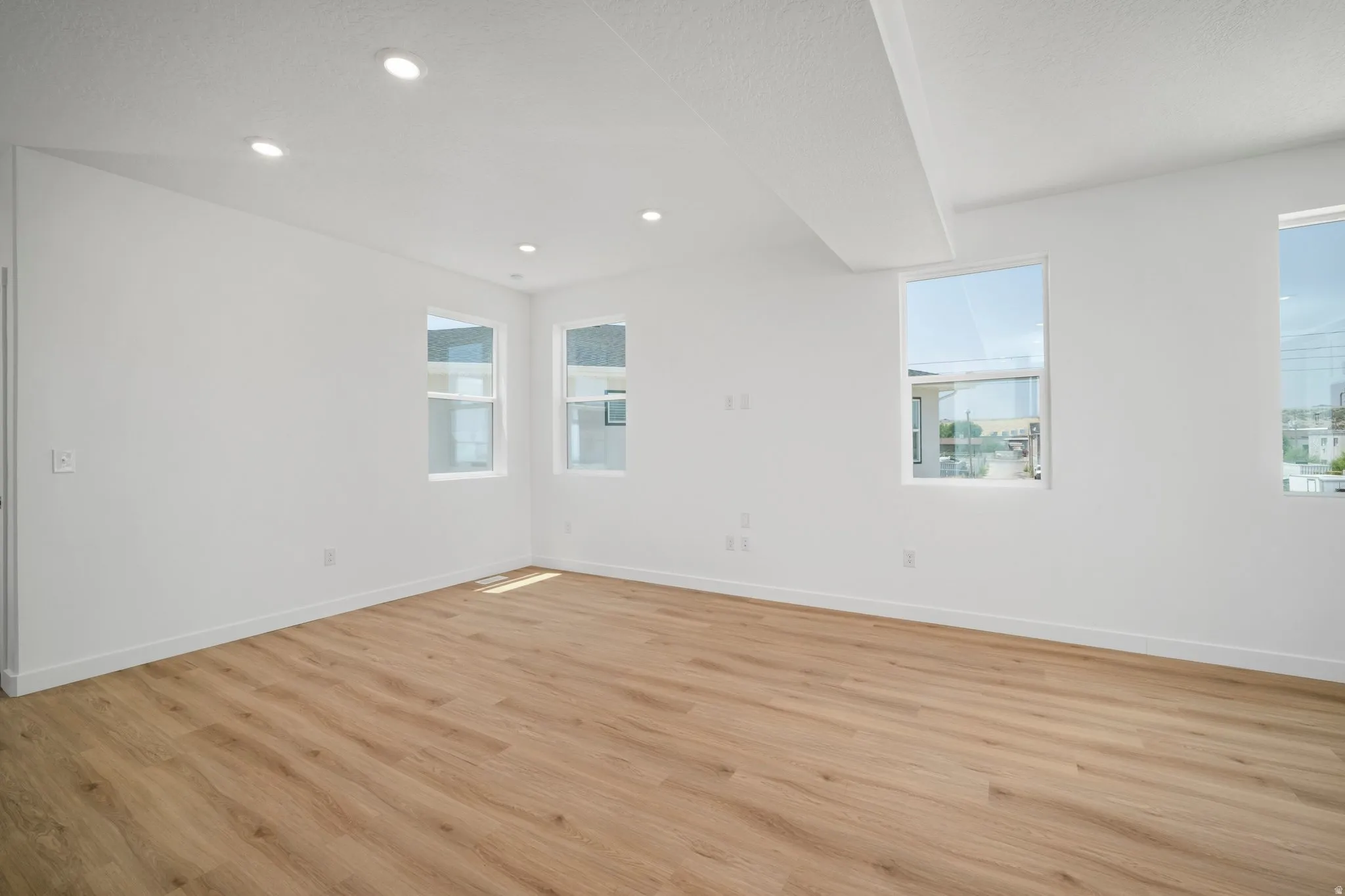 Recessed ceiling lighting, multiple windows, wood-finish flooring, white walls, and a white ceiling
