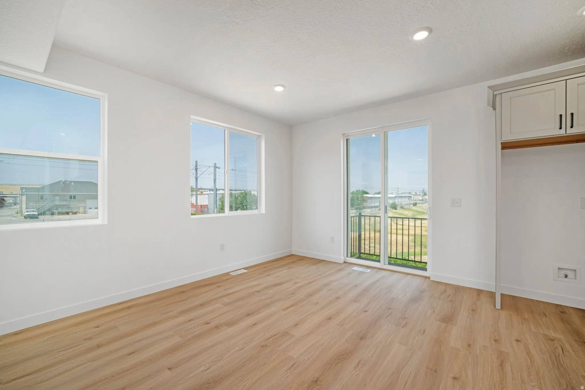 Wood-finish flooring, recessed lighting, white walls, built-in cabinetry, and sliding glass doors to a balcony