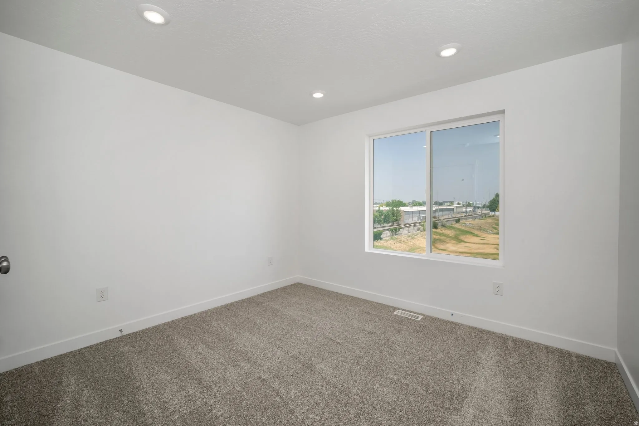 Recessed ceiling lighting, white walls, carpeted flooring, and a large window with white framing