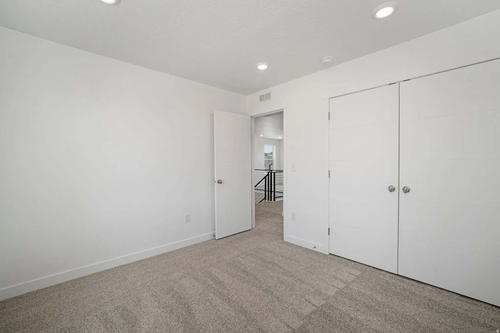 Recessed lighting, light-toned carpeting, white walls, white trim, and a white bi-fold closet door