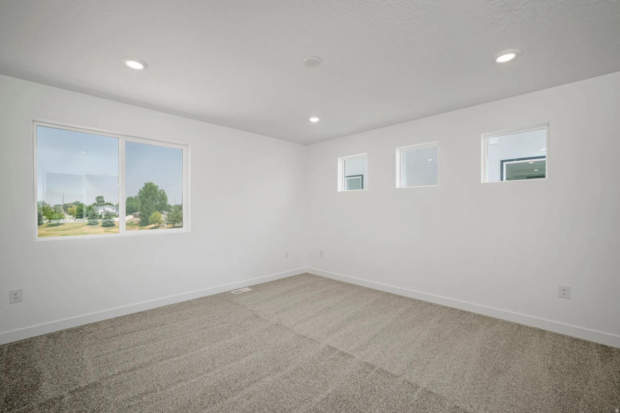 Recessed ceiling lighting, white walls, carpet flooring, a large window, and three smaller windows