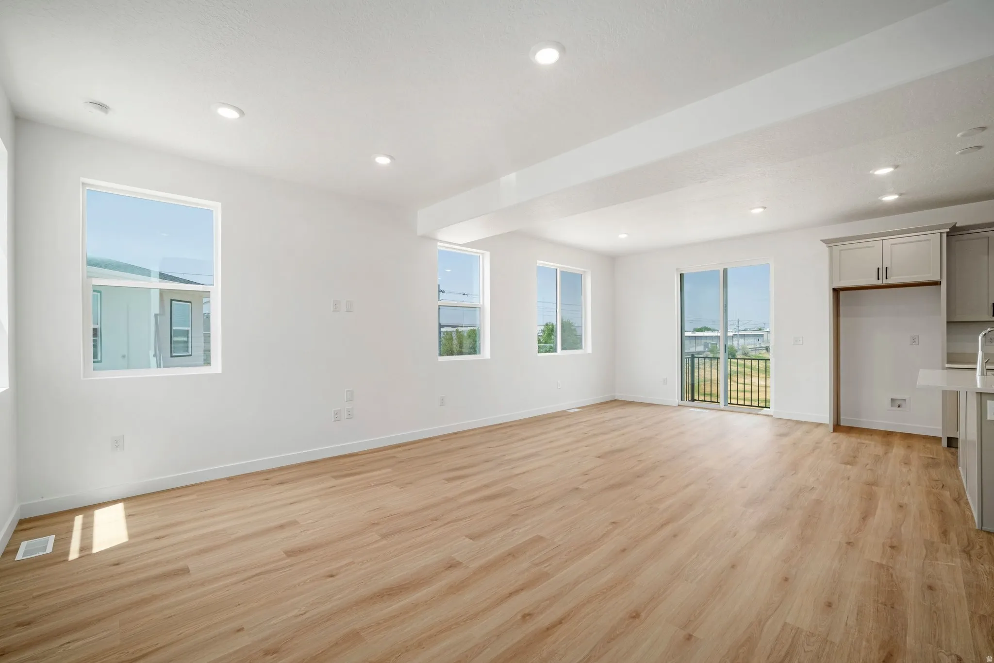 Open-concept living area featuring wood-finish flooring, recessed lighting, multiple windows, and a sliding glass door leading to a balcony