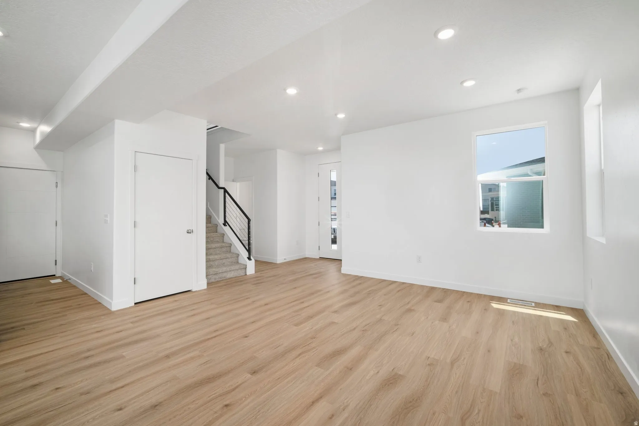 Recessed lighting, light wood-finish flooring, white painted walls, and a modern staircase with black metal railings