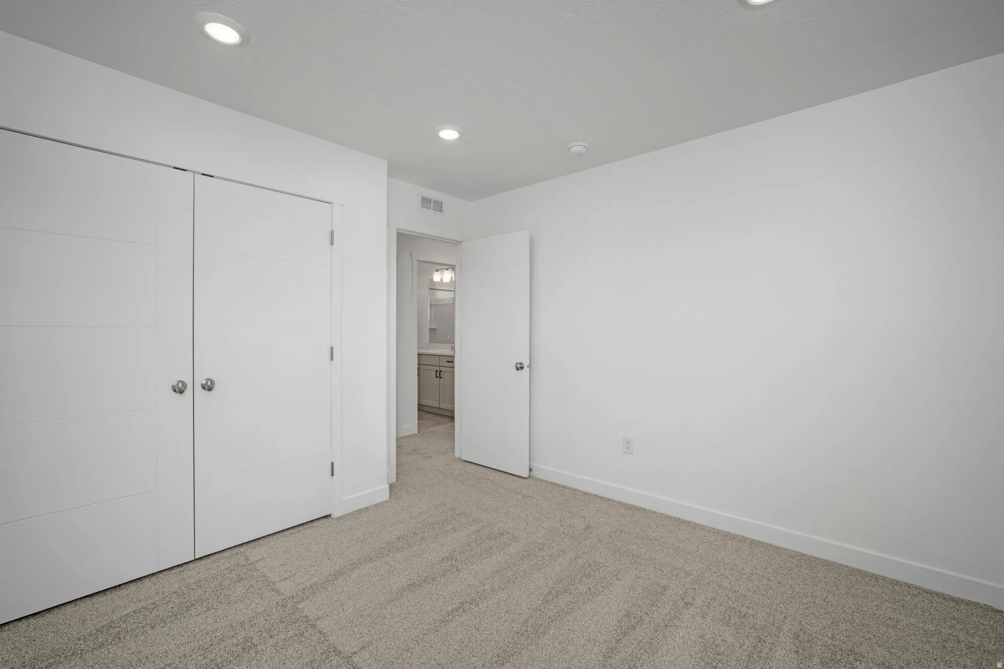 Recessed ceiling lighting, light-toned carpeting, modern bi-fold closet doors, white walls, and a white door with silver hardware