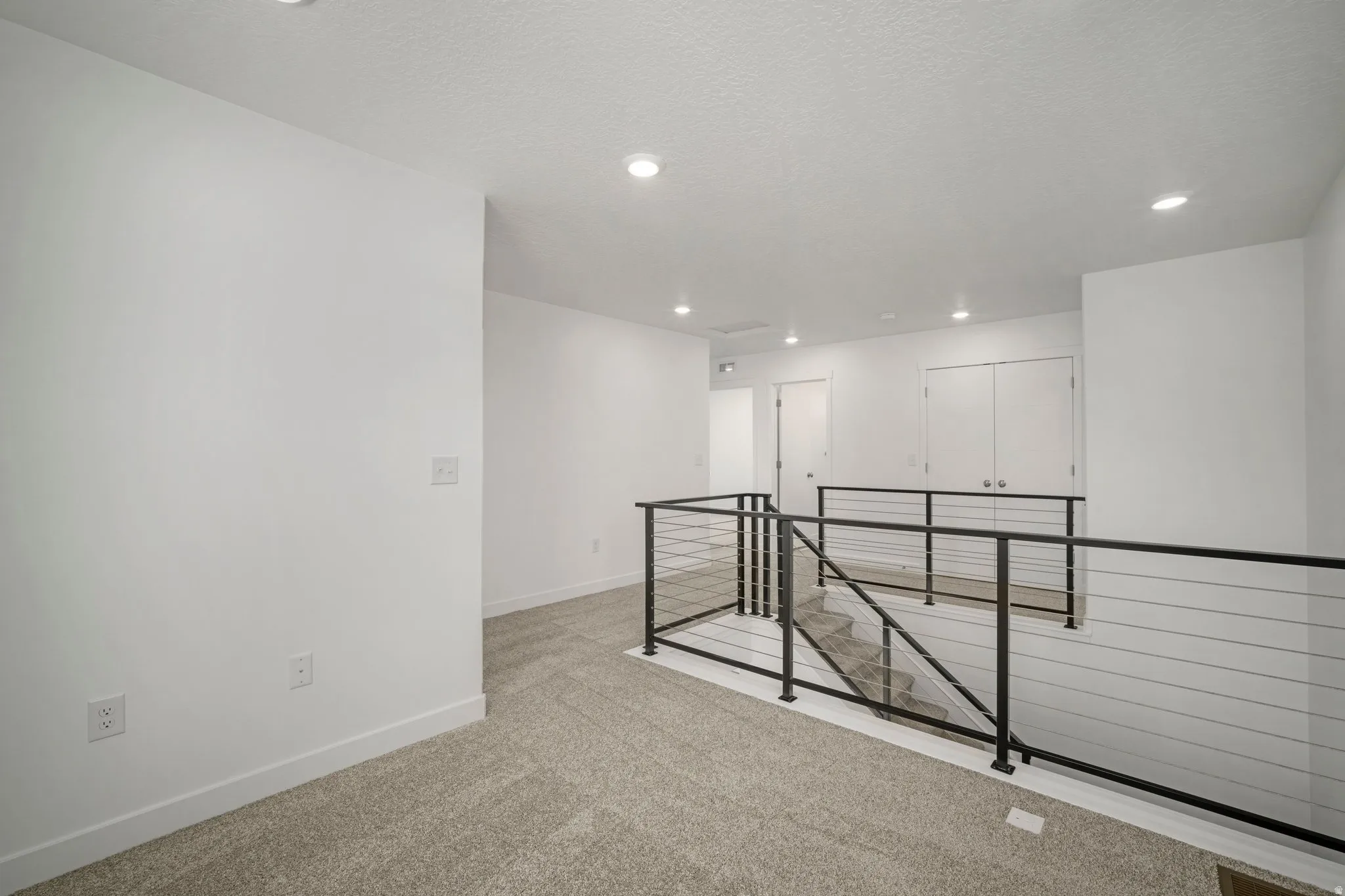 Carpeted landing with recessed lighting, white walls, and a modern cable railing system