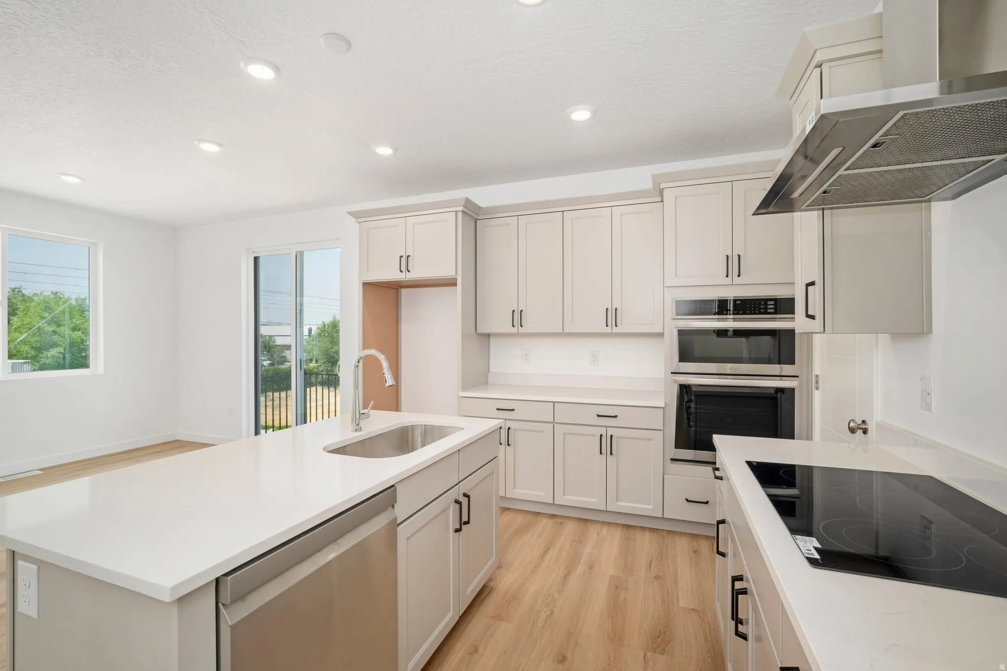 Kitchen featuring a central island with an undermount sink, built-in stainless steel dishwasher, light-toned cabinetry, and light wood-finish flooring