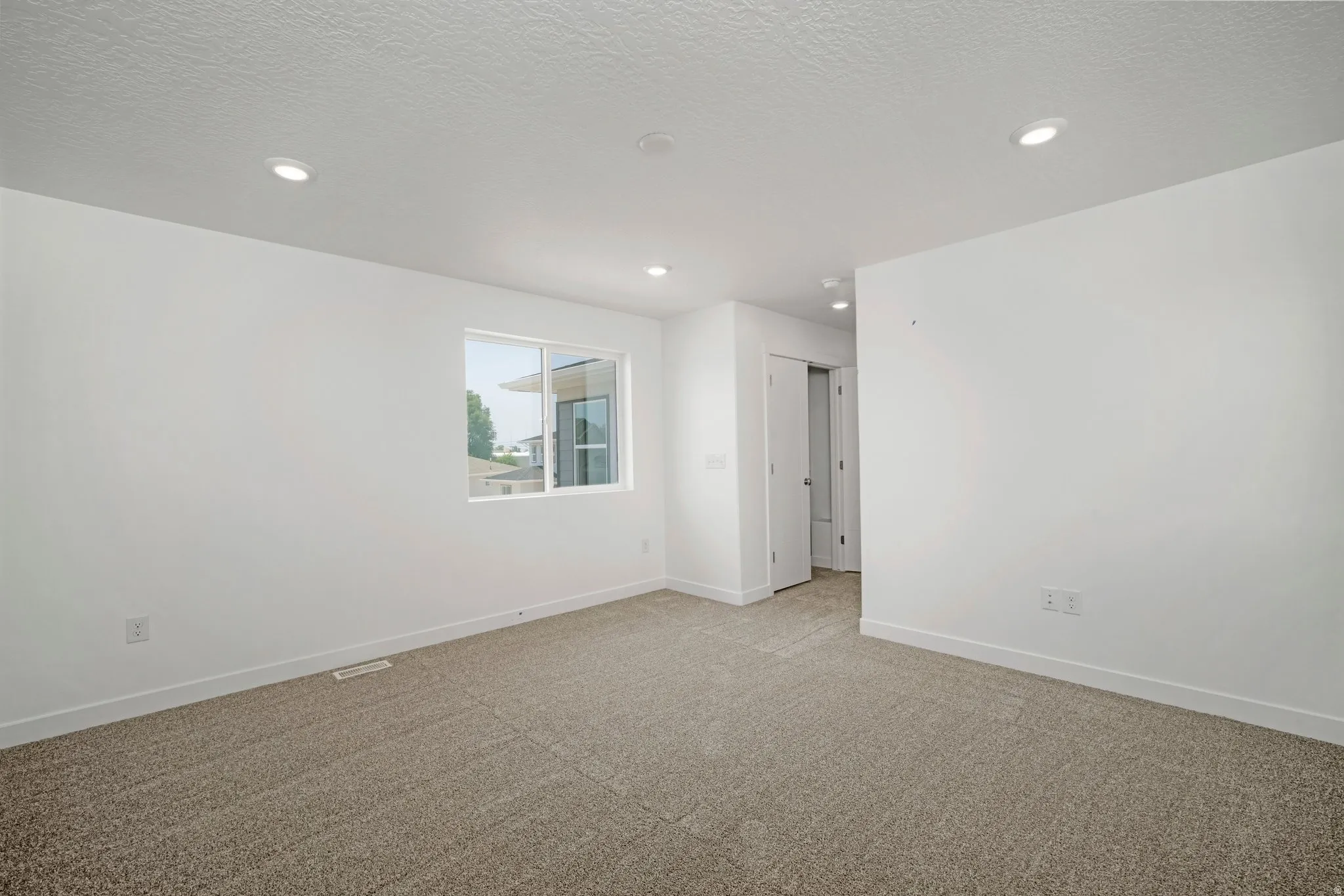 Recessed lighting, neutral-toned carpeting, white walls, and a sliding window