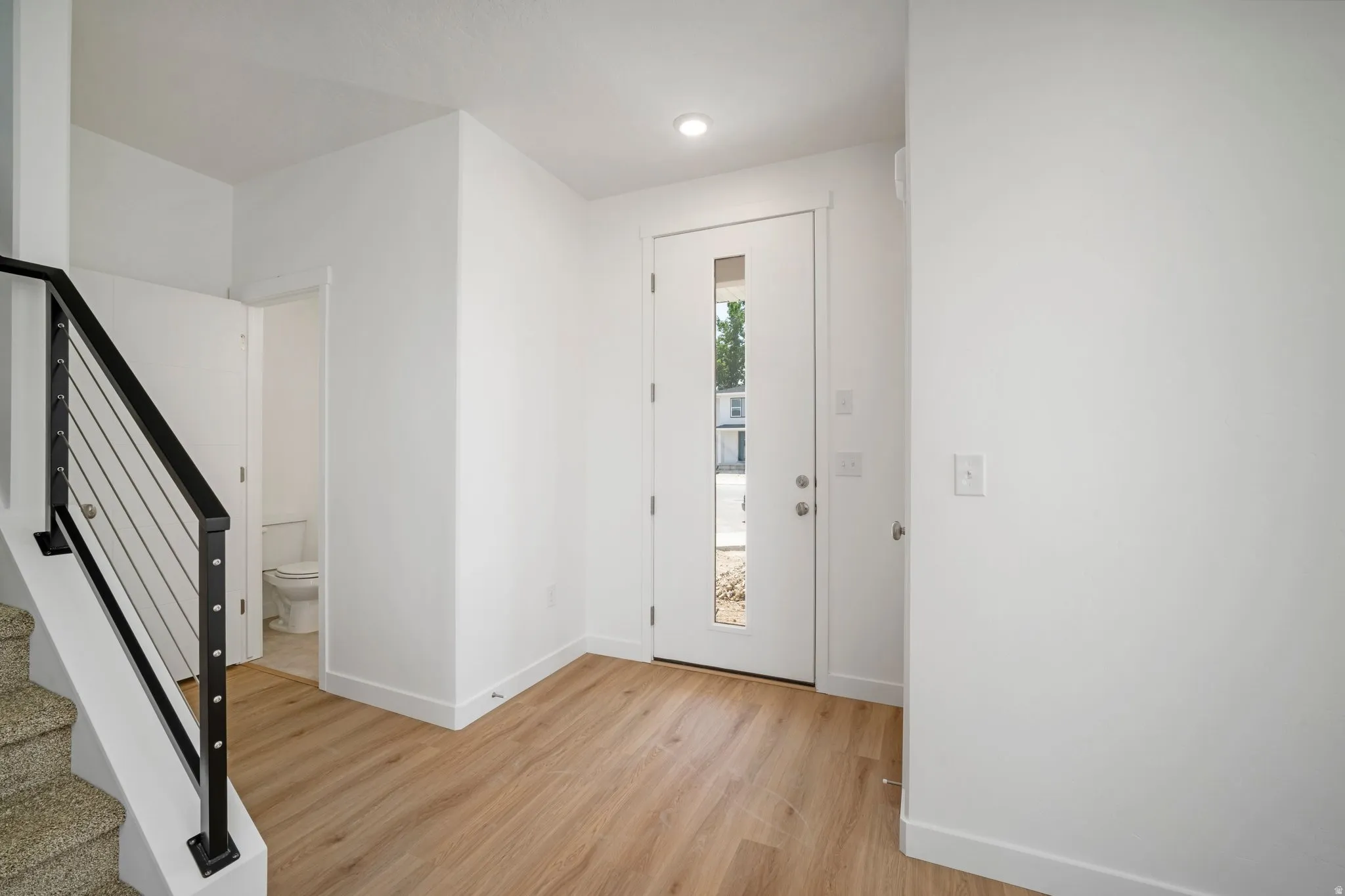 Hardwood-finish flooring throughout the entry, contemporary front door with vertical pane of glass, recessed lighting, and cable railing system on the staircase