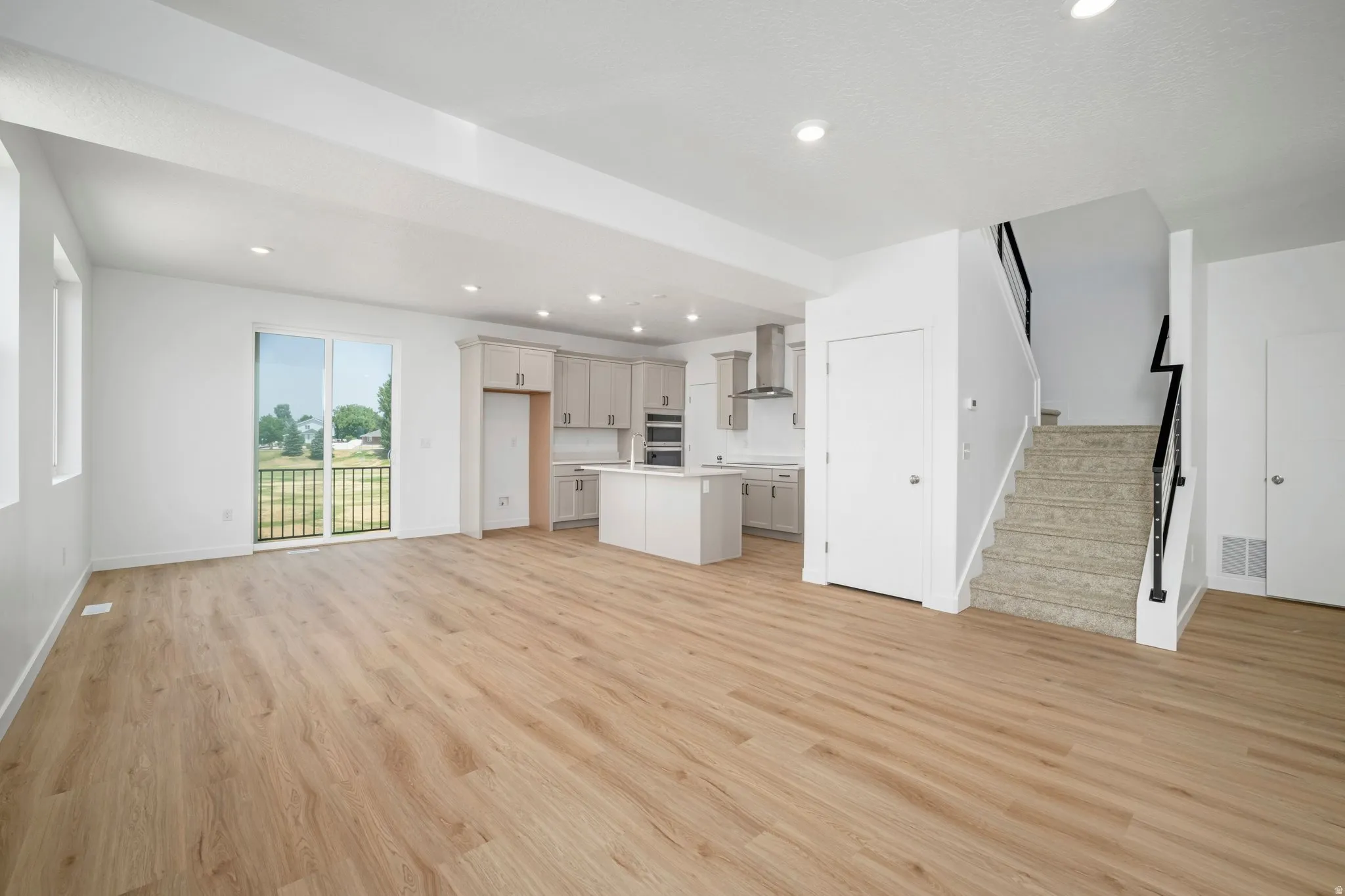 Open-concept living area with wood-finish flooring, recessed lighting, and sliding glass door access to a balcony