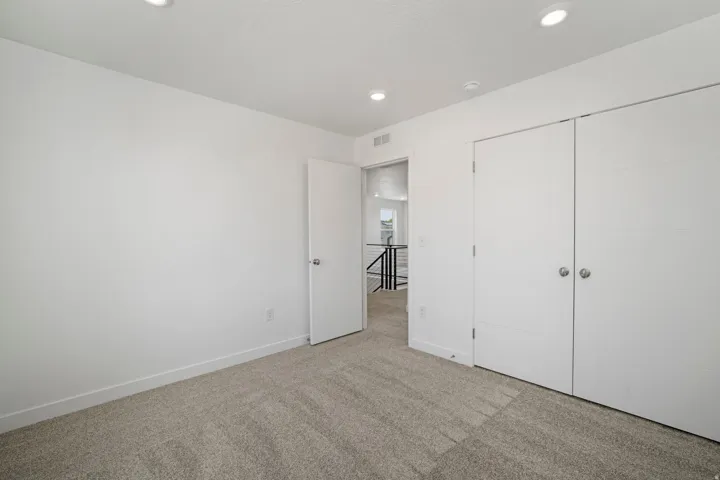 Recessed lighting, light-toned carpeting, white walls, white trim, and a white bi-fold closet door
