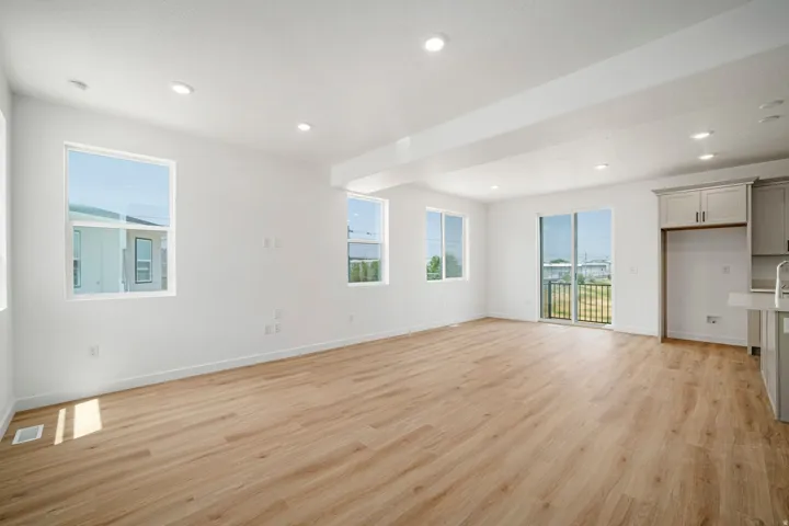 Open-concept living area featuring wood-finish flooring, recessed lighting, multiple windows, and a sliding glass door leading to a balcony