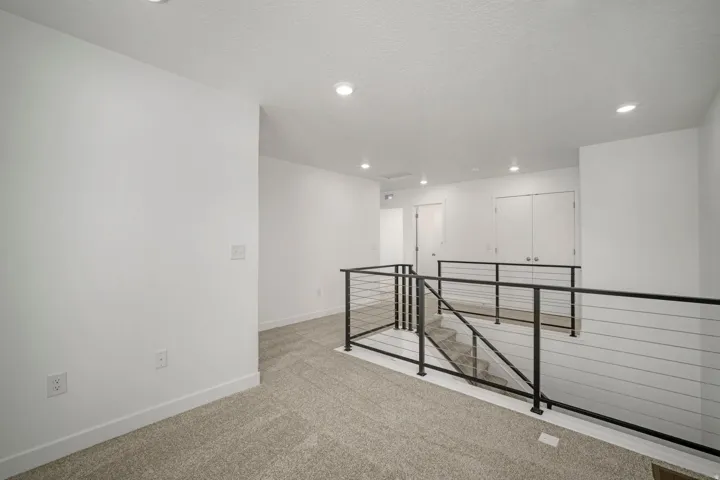 Carpeted landing with recessed lighting, white walls, and a modern cable railing system