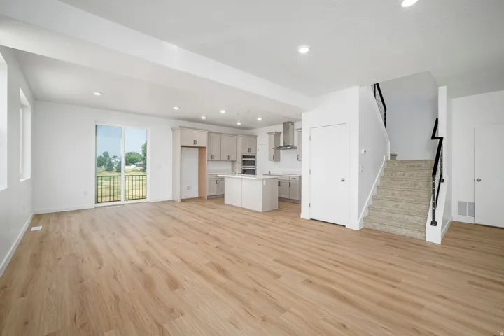 Open-concept living area with wood-finish flooring, recessed lighting, and sliding glass door access to a balcony