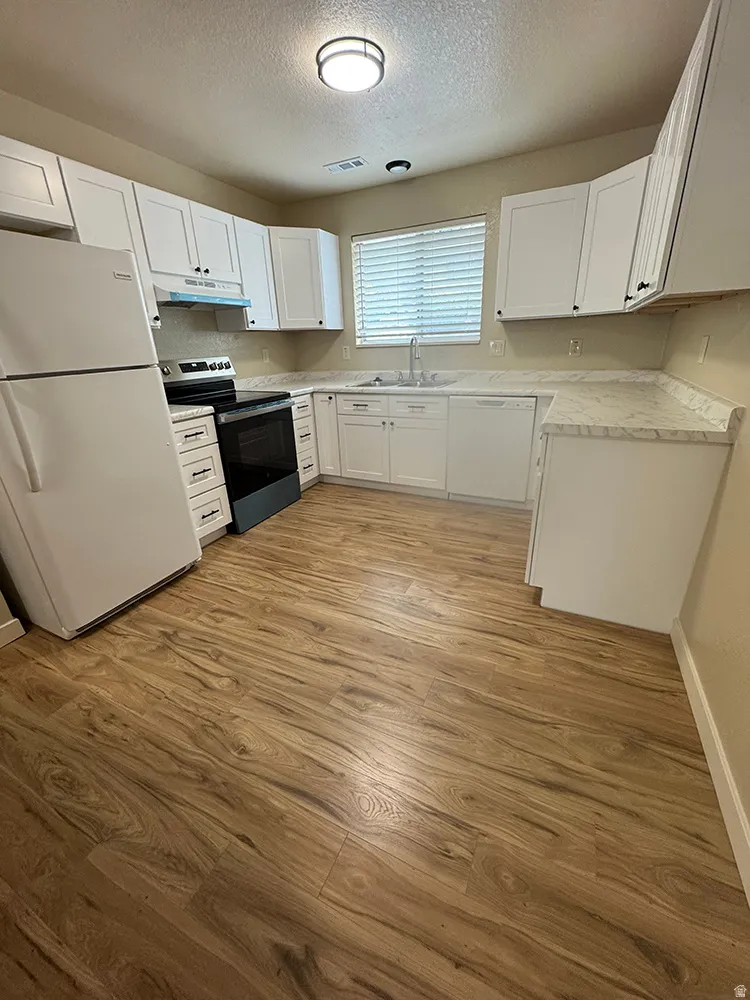 Kitchen featuring white cabinetry, wood-finish flooring, white appliances, and light-toned countertops