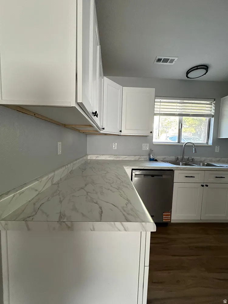White cabinetry with black hardware, marble-look countertops, stainless steel dishwasher, and wood-finish flooring